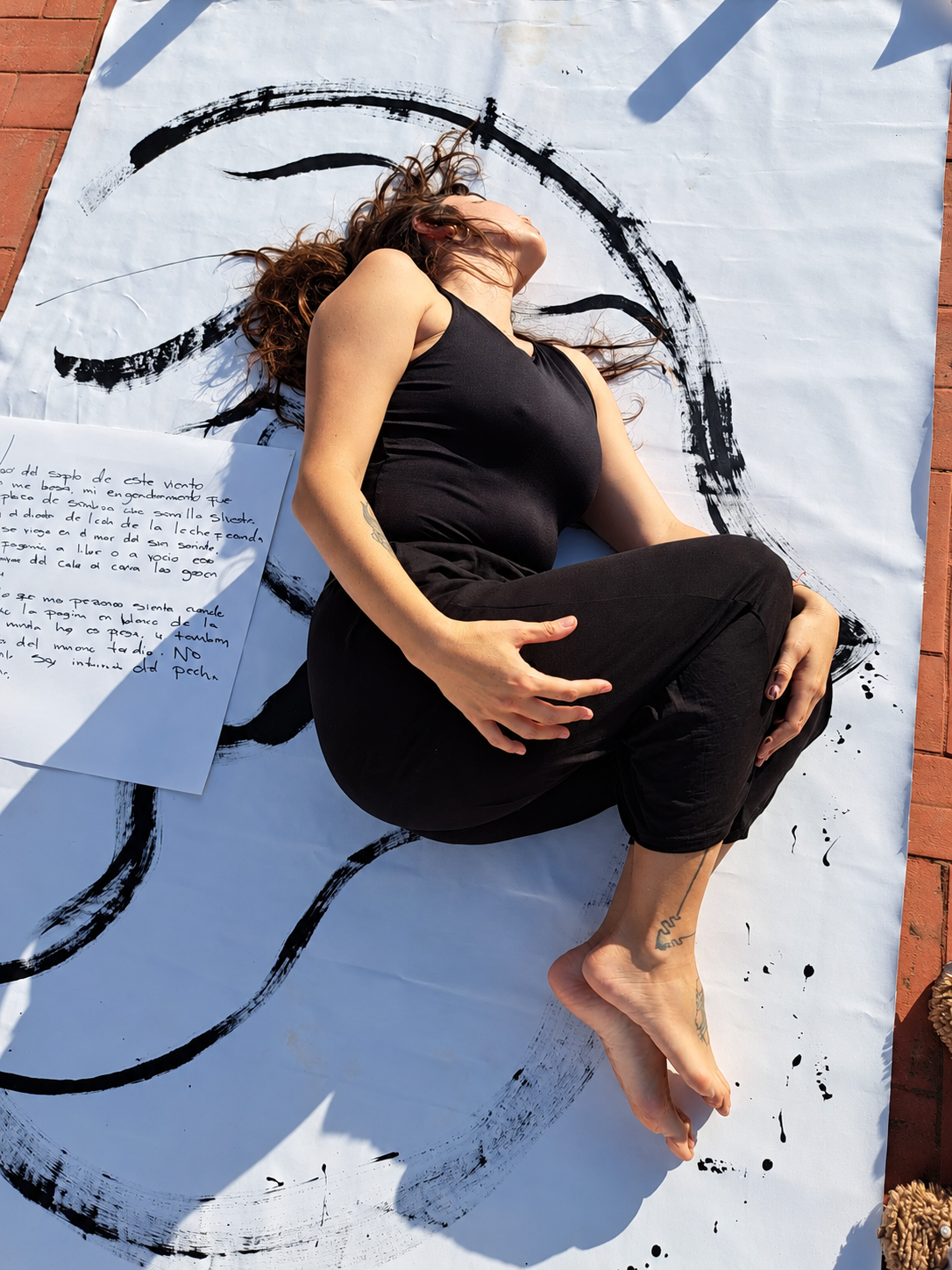 Viviana Gaviria Baena lying on a white canvas with black painterly brushstrokes